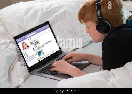 Garçon d'écouter de la musique tout en discutant sur le site de réseautage social, Using Laptop Banque D'Images
