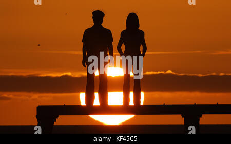 Le soleil se lève au-dessus de la sculpture en couple de Sean Henry sur la côte de la mer du Nord à la baie de Newbiggin, dans le Northumberland. Banque D'Images