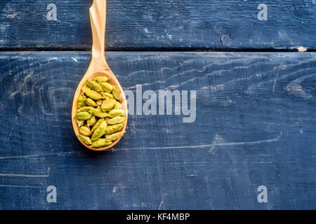 Fermer en vert graines de cardamome dans la cuillère en bois sur la surface en bois foncé Banque D'Images