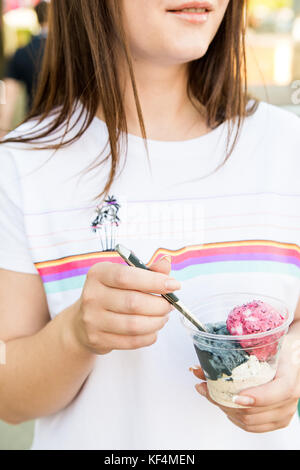 Close up female hands holding plastique verre avec trois boules de glaces et cuillère Banque D'Images