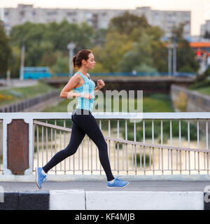 Young smiling woman running sportive sur le pont le matin. fitness petite fille jogging en ville Banque D'Images