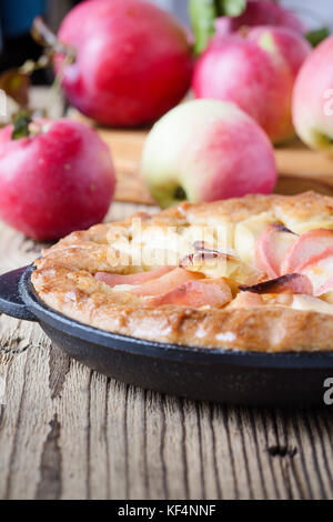 Tarte aux pommes faite maison cuit dans la poêle en fonte et des pommes mûres sur table en bois rustique Banque D'Images