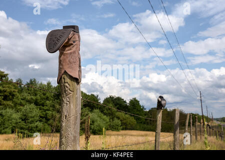 Cowboy boot sur un poteau de clôture de barbelés avec ciel dramatique. concepts pourraient inclure la culture, les traditions rurales, la vie dans l'ouest, de l'humour, d'autres. Banque D'Images