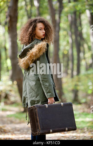 Cheveux bouclés teen girl avec valise rétro posant en forêt d'automne Banque D'Images