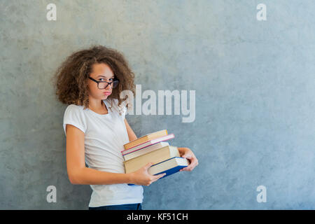 Portrait of teenage girl avec des lunettes se dresse à côté du mur et détient plusieurs livres Banque D'Images