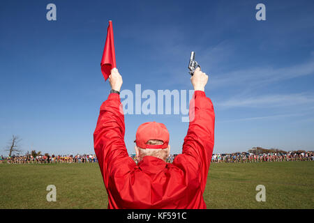 Homme habillé tout en rouge debout avec son dos à l'appareil face à un champ de concurrents brandissant une arme de démarrage et d'un drapeau comme il se prépare à lancer une Banque D'Images