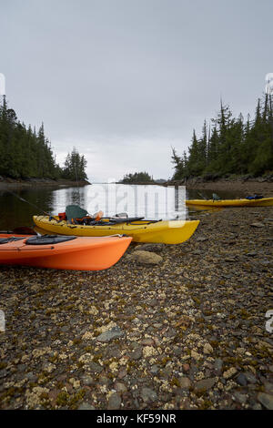 Kayaks échoué sur un rivage rocailleux dans la lumière du soir avec de l'eau tranquille et premier plan copy space Banque D'Images