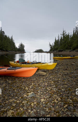 Kayaks échoué sur un rivage rocailleux dans la lumière du soir avec de l'eau tranquille et premier plan copy space Banque D'Images