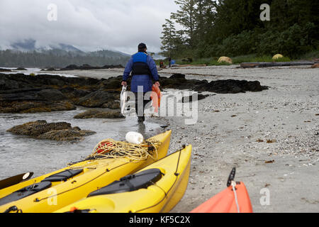 Fisherman transportant ses prises le long d'une plage de l'appareil photo avec les kayaks jaunes à l'avant-plan Banque D'Images