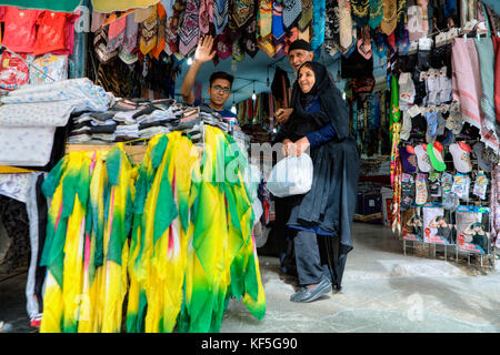 Shiraz, Iran - 19 avril, 2017 : un couple de personnes âgées choisit les tissus dans un magasin de textile, un jeune vendeur forme aux touristes qui photographient lui. Banque D'Images