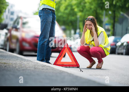 Les jeunes worried woman crouching près de signalisation triangulaire avec ventilées voiture sur street Banque D'Images