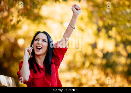 Heureux happy young woman listening de très bonnes nouvelles sur smartphone et être très heureux à l'automne la nature. Banque D'Images