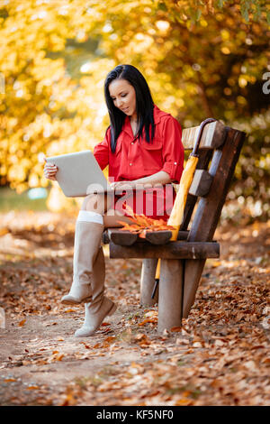 Jeune femme travaillant sur un ordinateur portable sur le banc du parc en automne. Banque D'Images