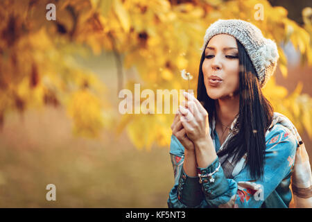 Portrait of young beautiful smiling positive young woman blowing dandelion in autumn park. Banque D'Images