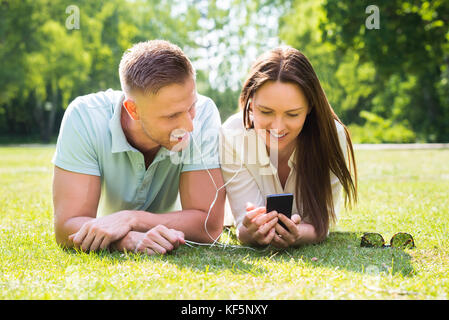 Happy Young Couple Lying On Grass à l'écoute de la musique sur téléphone mobile Banque D'Images
