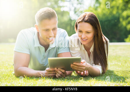 Jeune couple Lying On Grass Using Digital Tablet At Park Banque D'Images