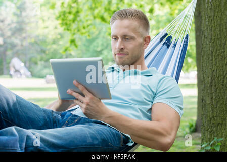 Man lying in hammock using digital tablet