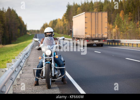 Femme sur une moto se dresse sur la route d'un pays près de l'autoroute passant camion de marchandises Banque D'Images