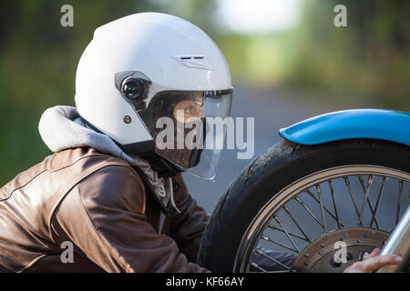 Femme dans un casque de moto serrant une roue à rayons de moto ressemble à un projecteur Banque D'Images