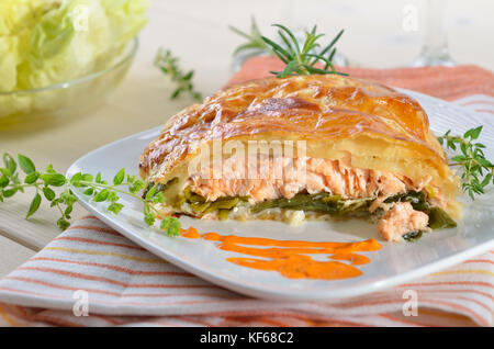 Filet de saumon sur les poireaux, cuit en pâte feuilletée, servi avec des fines herbes, sauce et salade Banque D'Images