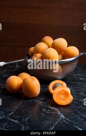 Organique mûres abricots en composition. passoire en acier dans un style rustique - jaune bio abricots juteux dans son ensemble et passoire en acier et des moitiés d'abricots o Banque D'Images