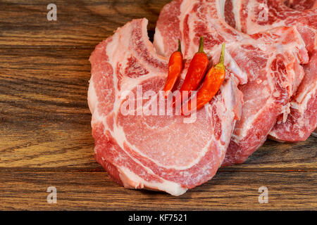 Côtelette de porc cru steak avec des ingrédients poivre, sel feuille sur une planche à découper en bois Vue de dessus Banque D'Images