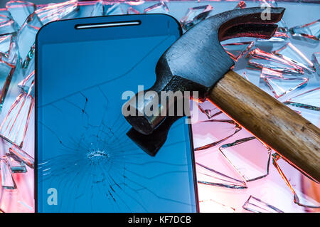 Noir cassé Smartphone avec écran brisé gisant sur des morceaux de verre brisé à l'aide d'un marteau au-dessus Banque D'Images