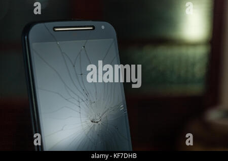 Moitié supérieure de noir cassé Smartphone avec écran fissuré allumé sur un fond sombre Banque D'Images