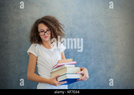 Portrait of teenage girl avec des lunettes se dresse à côté du mur et détient plusieurs livres Banque D'Images