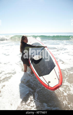 États-unis, Californie, Malibu, el pescador beach, une femme porte son paddleboard dans l'océan pacifique Banque D'Images