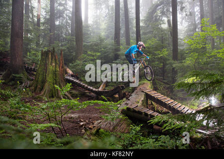 Canada, Vancouver, Colombie-Britannique, mountain biker Andrew Baker obtient l'air sur un sentier dans la forêt tropicale, north vancouver Banque D'Images