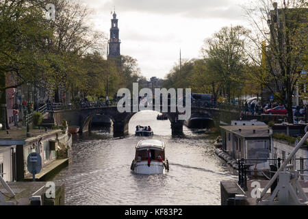 Des bateaux naviguant sur un canal à Amsterdam avec house boats de chaque côté et le westertoren dans la distance Banque D'Images