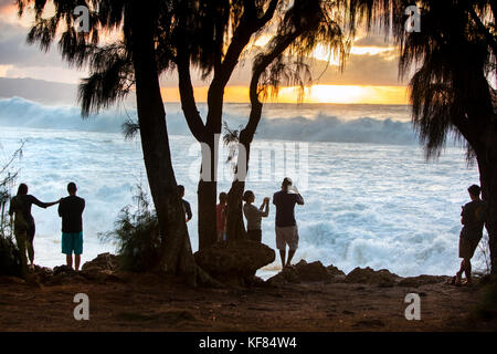 Hawaii, Oahu, côte-nord, spectateurs de regarder un grand rouleau de houle dans au coucher du soleil à pupukea Beach Park sur la Côte-Nord Banque D'Images