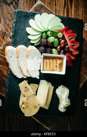 Assortiment de fromages, des tranches de pain frais et de fruits à bord sombre Banque D'Images