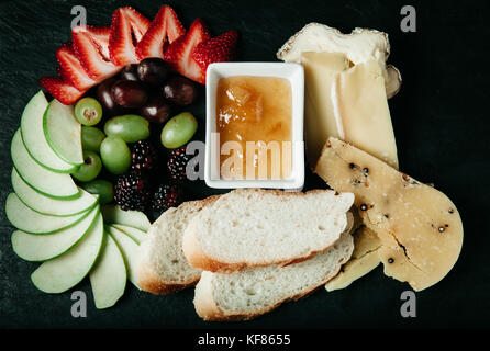 Assortiment de fromages, des tranches de pain frais et de fruits sur fond sombre Banque D'Images