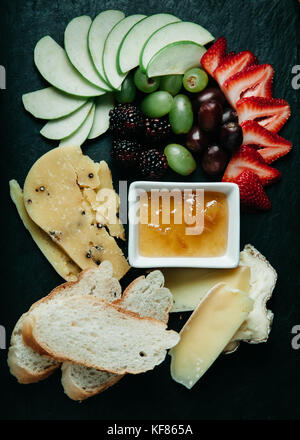 Assortiment de fromages, des tranches de pain frais et de fruits à bord sombre Banque D'Images