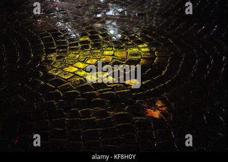 Réflexions de l'éclairage au néon en vert sur la rue humides et pluvieuses de cobblestone. closeup photo horizontale la nuit. soir tourné dans le noir. Banque D'Images