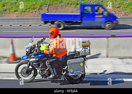 Close up of Triumph Motor bike rider conduite le long de l'autoroute à trois voies UK wearing high vis veste et un casque dans la section Travaux routiers Banque D'Images