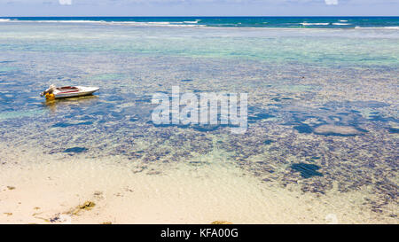 Petit bateau amarré dans les eaux tropicales peu profondes avec les coraux et reef visible dans la distance Banque D'Images