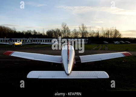 Un Piper PA-28-161 Cabair Cadet, un guerrier Cherokee et Grumman American AA-5B Tiger garé sur le tarmac avec l'école de pilotage derrière Banque D'Images