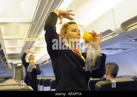 Hôtesses de l'air montrant comment utiliser le masque à oxygène pendant le briefing de sécurité dans la cabine de classe économique d'un Titan Airways Boeing 737-300 Banque D'Images