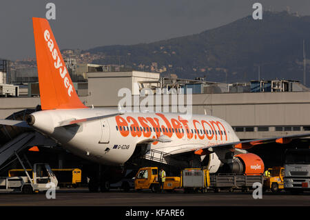 Un Airbus A319 d'easyJet garé au terminal avec escaliers, des camions et des chariots à bagages Banque D'Images