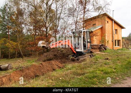 Mini pelle sur chantier. construction d'une maison de famille près d'une forêt Banque D'Images