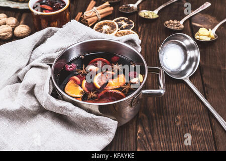 Vin chaud dans une poêle avec une cuillère de fer, derrière les ingrédients dans les cuillères sur un fond en bois brun Banque D'Images