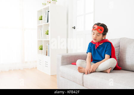 Jolie petite fille cute kid portant manteau rouge avec masque de jouer en tant que super-héros fatigué assis sur salon canapé lit pour dormir. Banque D'Images