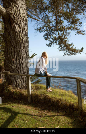 États-unis, Californie, Big Sur, Esalen, femme assise sur la clôture près de la maison de ferme et apprécie le soleil et la vue sur le Pacifique, l'Institut Esalen Banque D'Images
