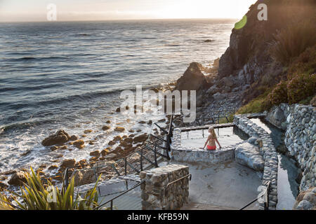 États-unis, Californie, big sur, esalen, une femme assise sur le bord de la source chaude aux bains et prend dans la soirée, l'Institut Esalen Banque D'Images