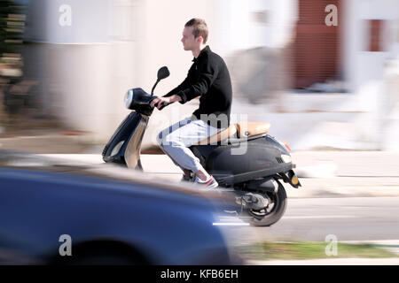 Un jeune qui fait un scooter à vitesse rapide le long de la route. Le cliché est panoramique, ce qui donne une impression de mouvement. Prise près de Rhodes, Rhodes, Grèce Banque D'Images