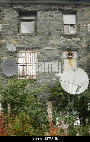 Antennes paraboliques à l'arrière d'une maison mitoyenne en pierre abandonnée. Banque D'Images