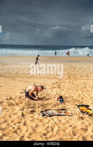 Usa, Hawaii, Oahu, northshore, un jeune couple burry mutuellement dans le sable par pipe-line Banque D'Images